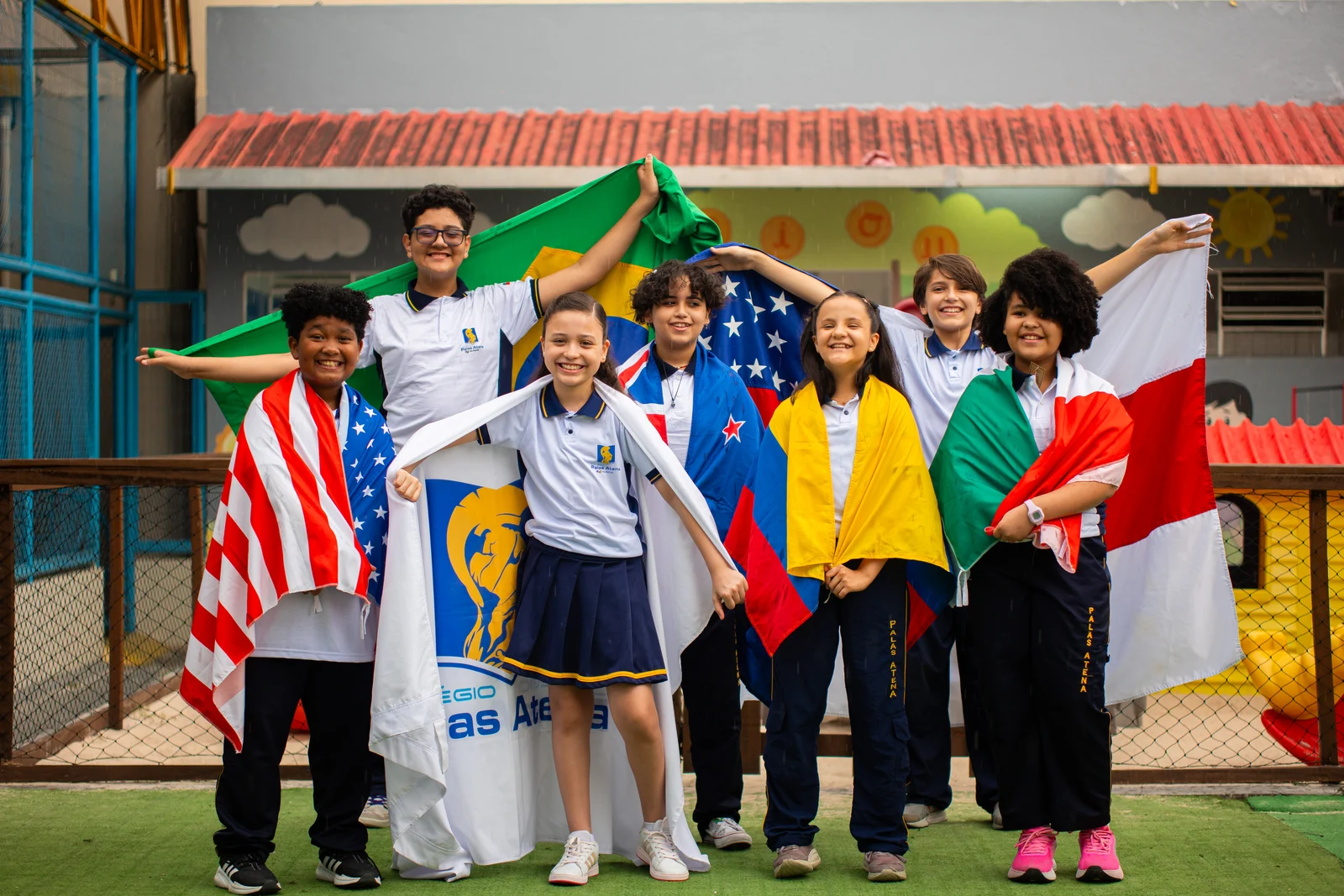 Alunos do Palas Atena segurando bandeiras internacionais e o brasão da escola celebrando a educação global