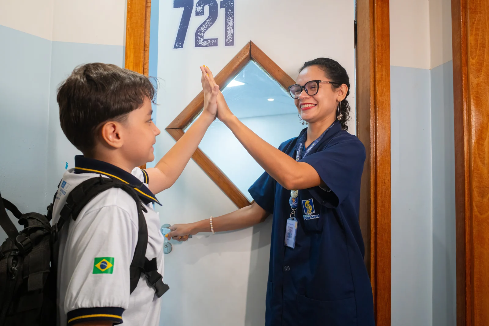 Professora cumprimentando aluno com um high five na entrada da sala de aula