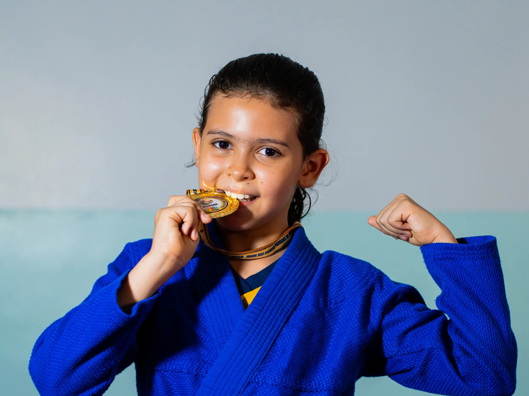 Aluna do Palas Atena de quimono de judô, mordendo uma medalha