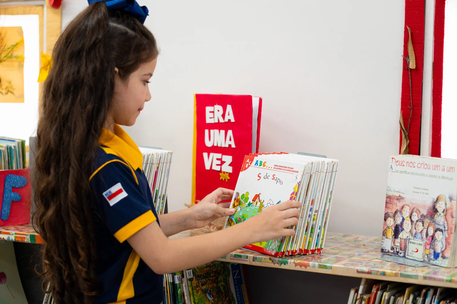 Aluna escolhendo livro na biblioteca infantil do projeto de leitura do Palas Atena